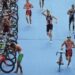 Triathleter springer med cyklar genom en blå växlingszon