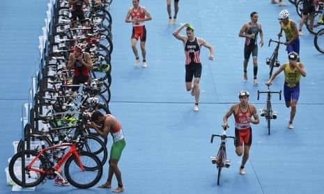 Triathleter springer med cyklar genom en blå växlingszon